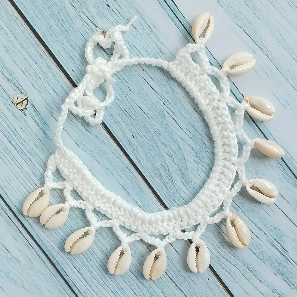 White crocheted necklace with shell pendants on a light blue wooden background