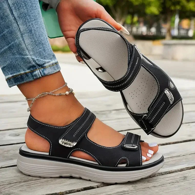 Person wearing black sandals with straps on a wooden floor.
