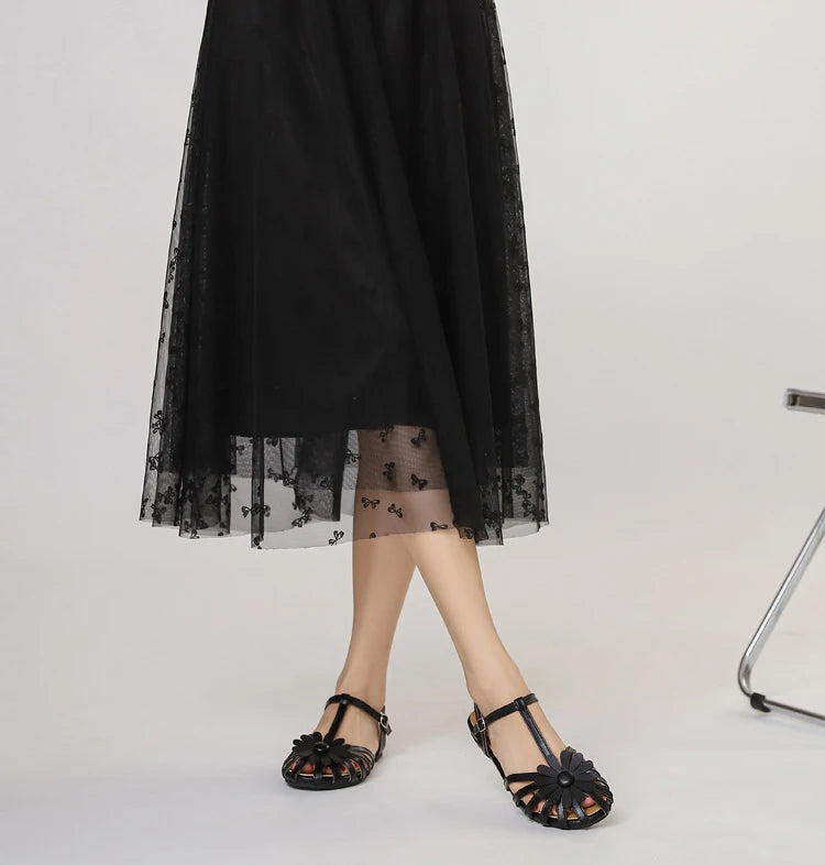 Person wearing a black dress with floral lace details on a plain background