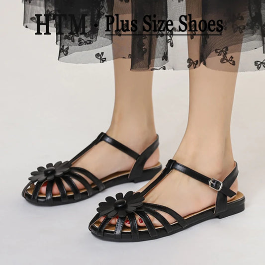 Black sandals with floral details worn by a person on a light background