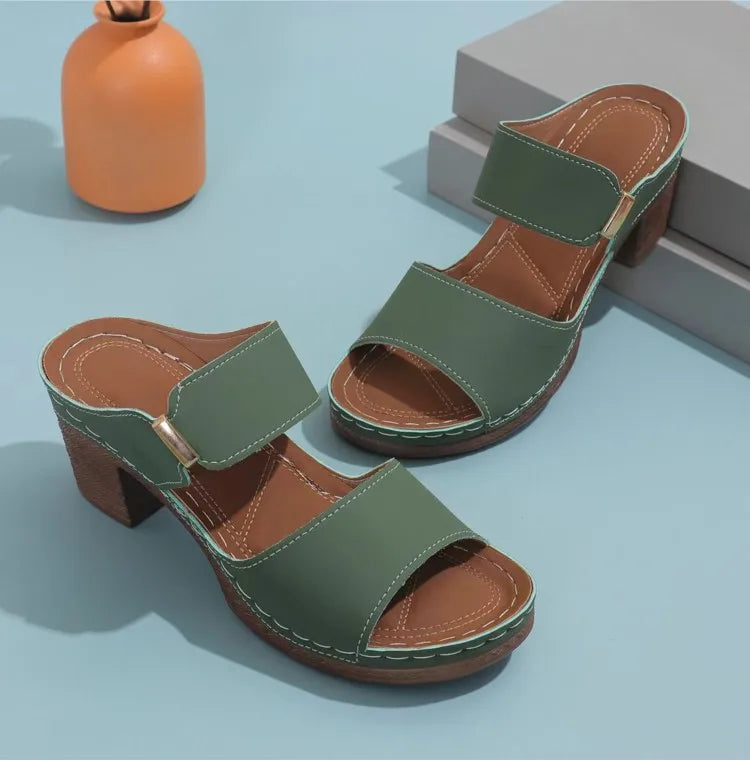 Green and brown sandals on a light blue surface with an orange vase in the background.