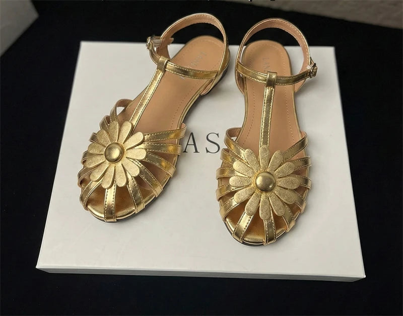 Pair of gold sandals with floral designs on a white surface