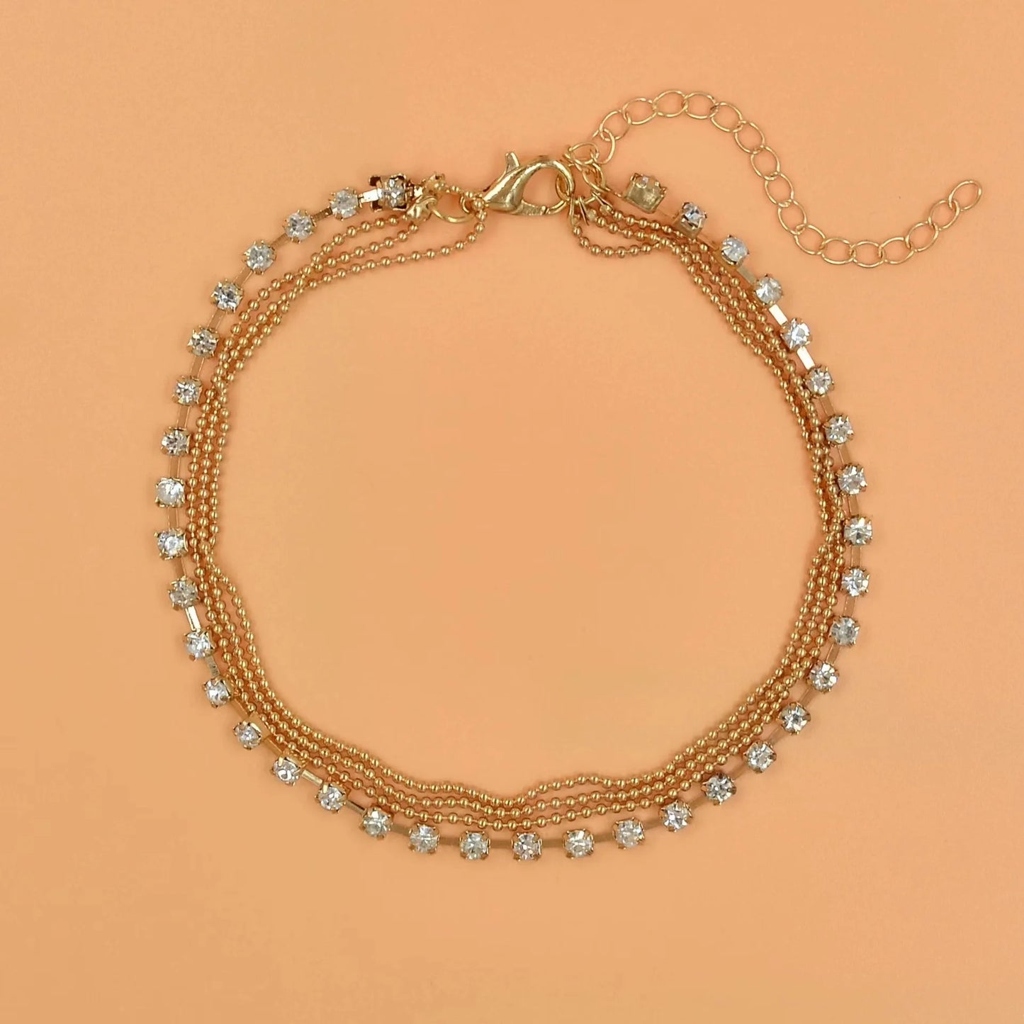 Gold bracelet with clear stones on a peach background